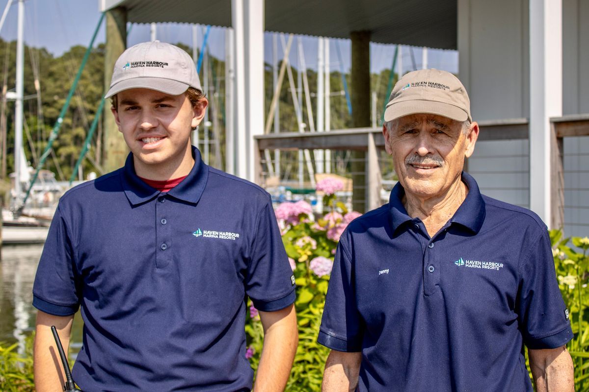 Two employees pictured outside in front of flowers and sailboats