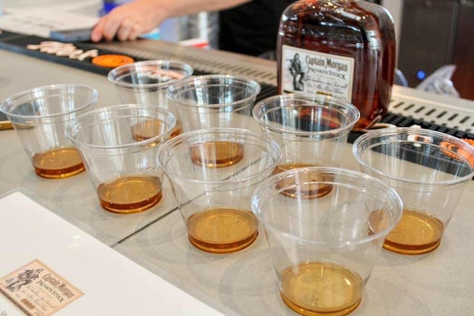 Plastic cups with rum samples on a tasting counter, with rum bottle in the background.