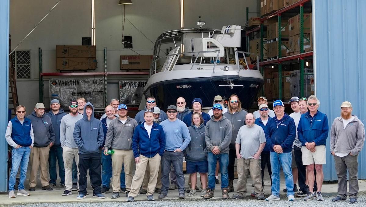 Outdoor group photo of marine technicians in front of large boat shop with its doors open