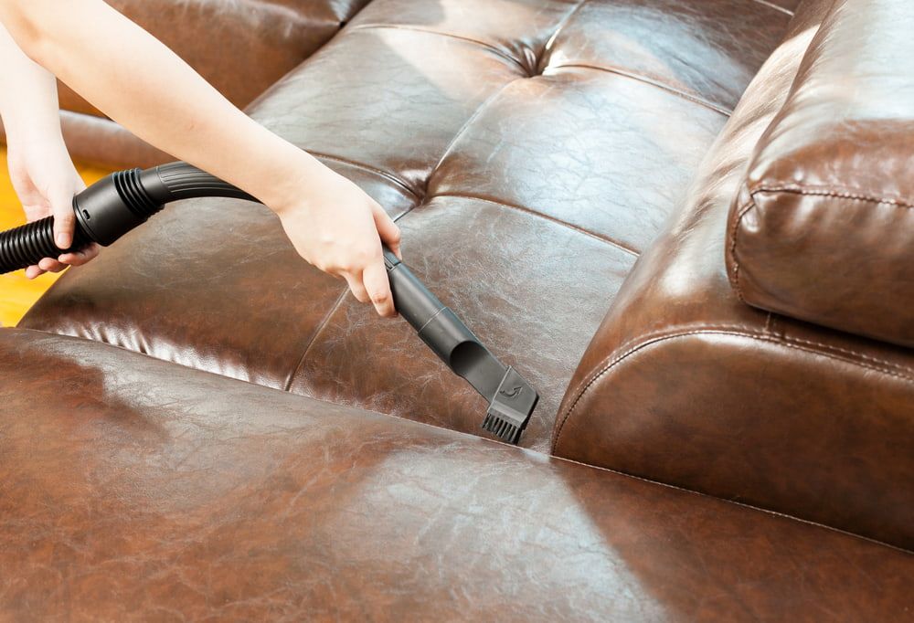 A Person is Cleaning a Brown Leather Couch With a Vacuum Cleaner — Clean Right Carpet Cleaning In Port Macquarie, NSW