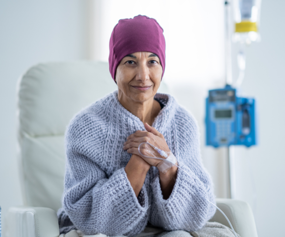Paziente seduto su una sedia da ambulatorio, con indosso un copricapo viola e un maglione grigio, con un supporto per flebo nelle vicinanze.