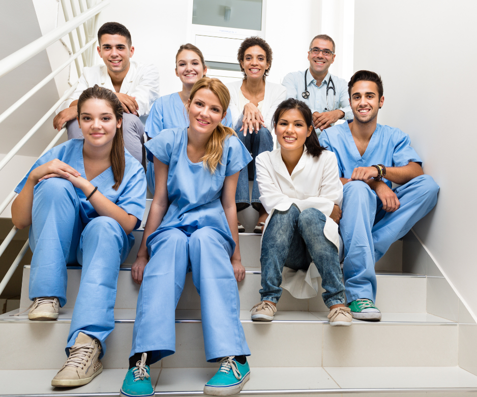 Sette operatori sanitari in camice seduti sulle scale, sorridono alla telecamera.