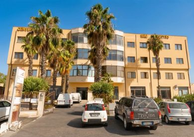 Palazzo residenziale con palme e auto parcheggiate di fronte, sotto un cielo limpido.