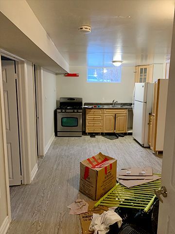 A kitchen in a basement with a stove , refrigerator , cabinets , and a box on the floor.