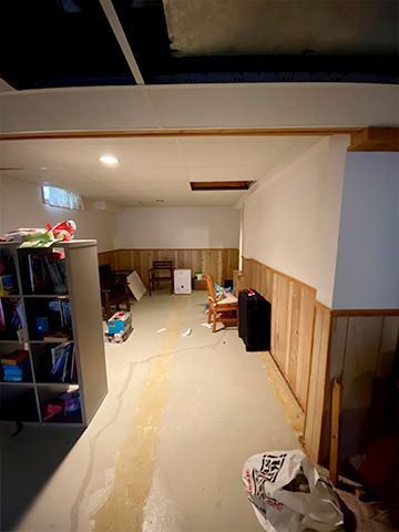 A basement with a flooded floor and a ceiling that has a hole in it.