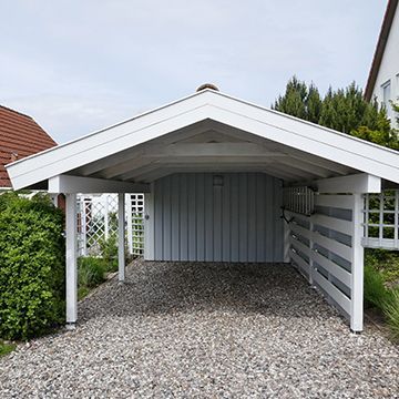 A carport is sitting on top of a gravel driveway next to a house.