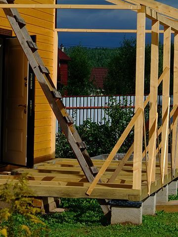 A wooden deck is being built in front of a yellow house.