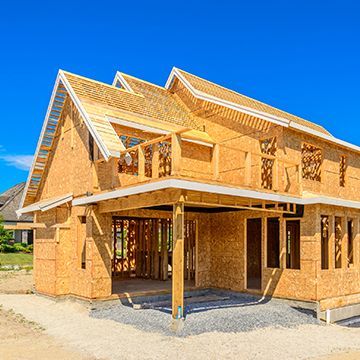 A wooden house is being built with a blue sky in the background.