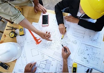 A group of people are sitting around a table looking at blueprints.