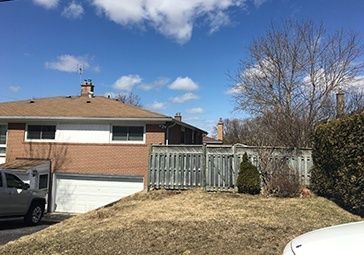A white car is parked in front of a brick house.