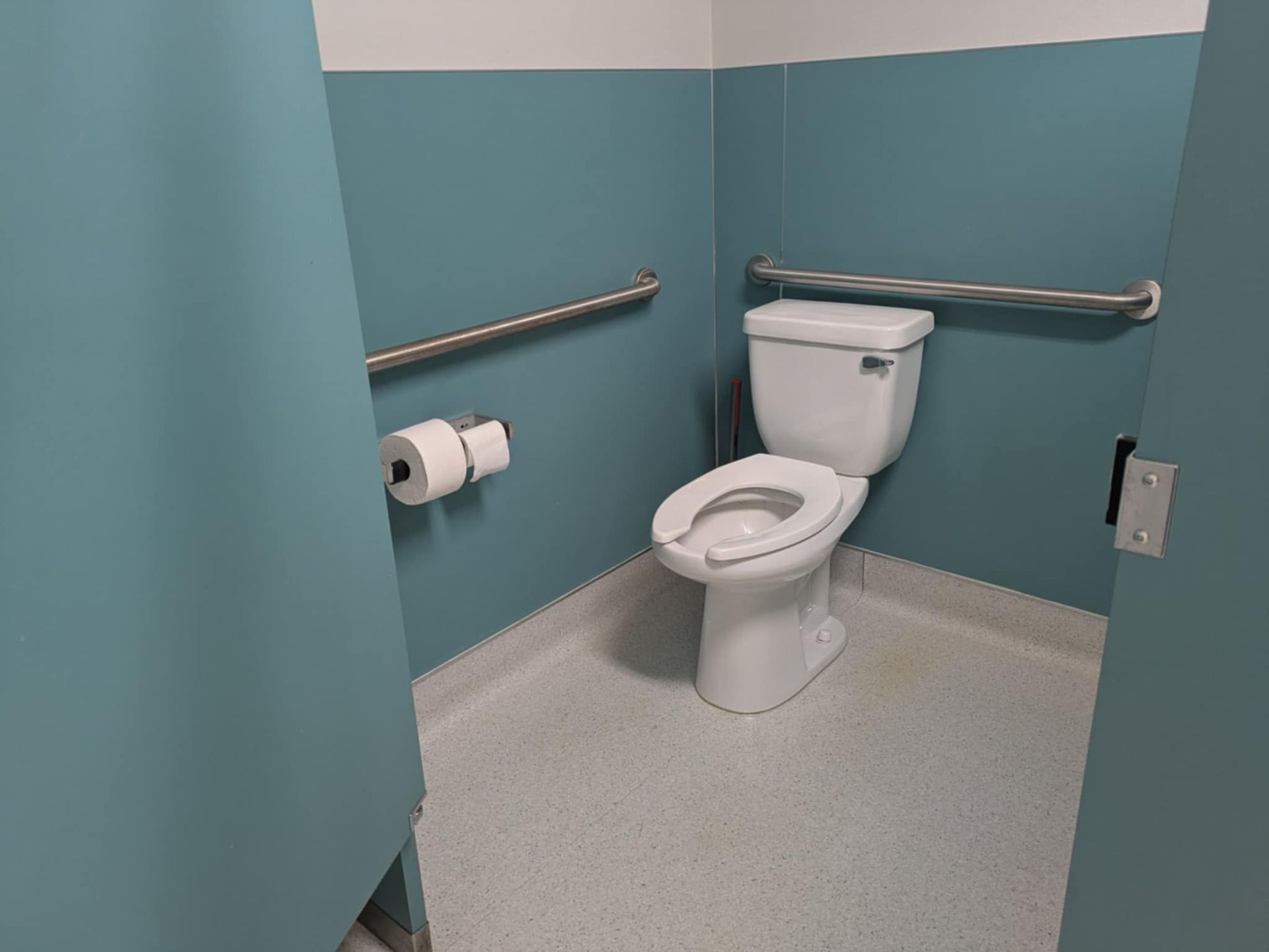 A stall in a public bathroom, that is large and has grab rails.