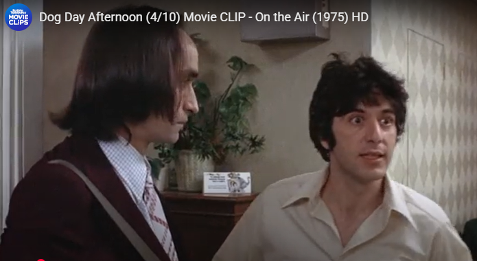 Two men talking in an office, one in a suit and one in a white shirt, with a TV title overlay.