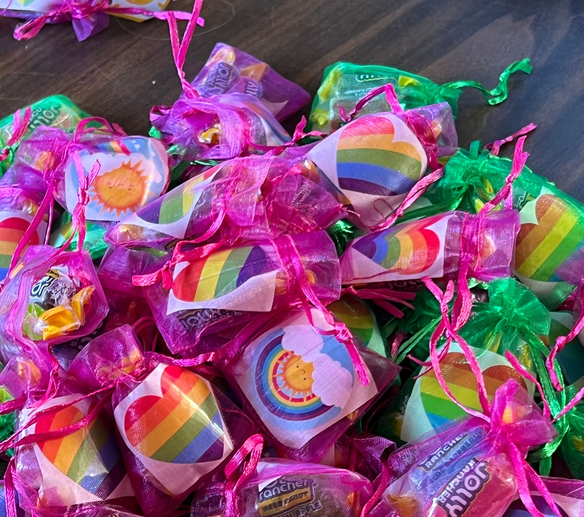 Colorful rainbow swirl candies in pink and green mesh wrappers on a dark wooden surface