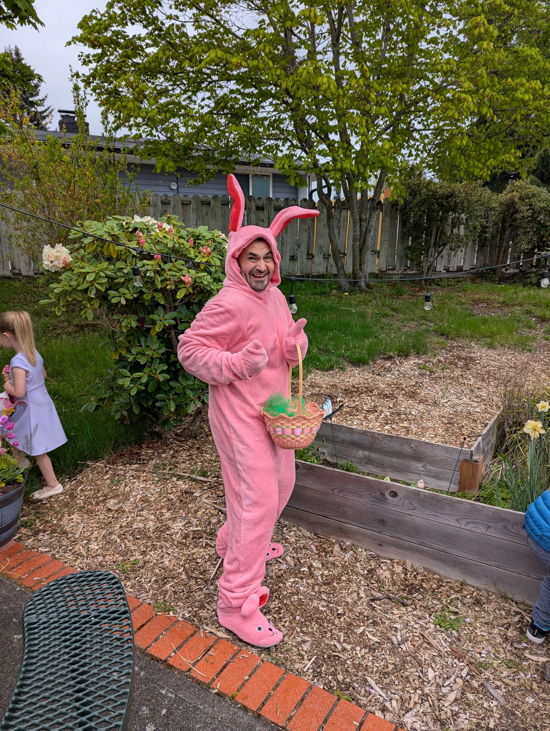 Person in a pink bunny costume holding a green basket in a garden.