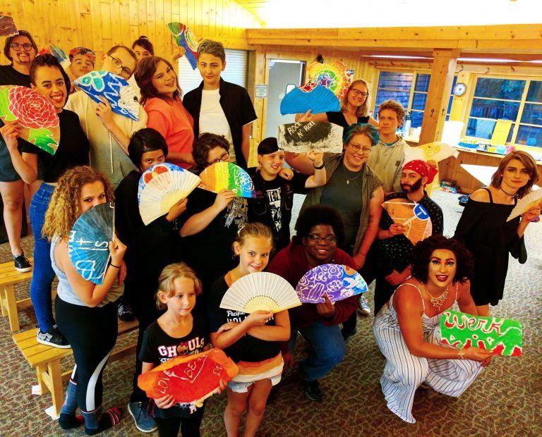 Group of people posing indoors with colorful decorated fans in a bright room