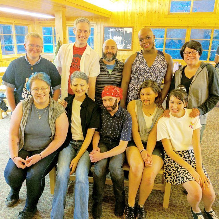Group of nine people posing indoors in a warmly lit room, smiling at the camera.