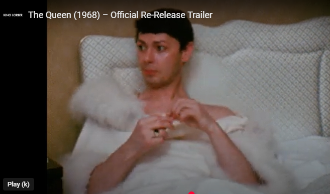 Person in a white bed looking to the side, hands clasped near chest, in a film trailer frame