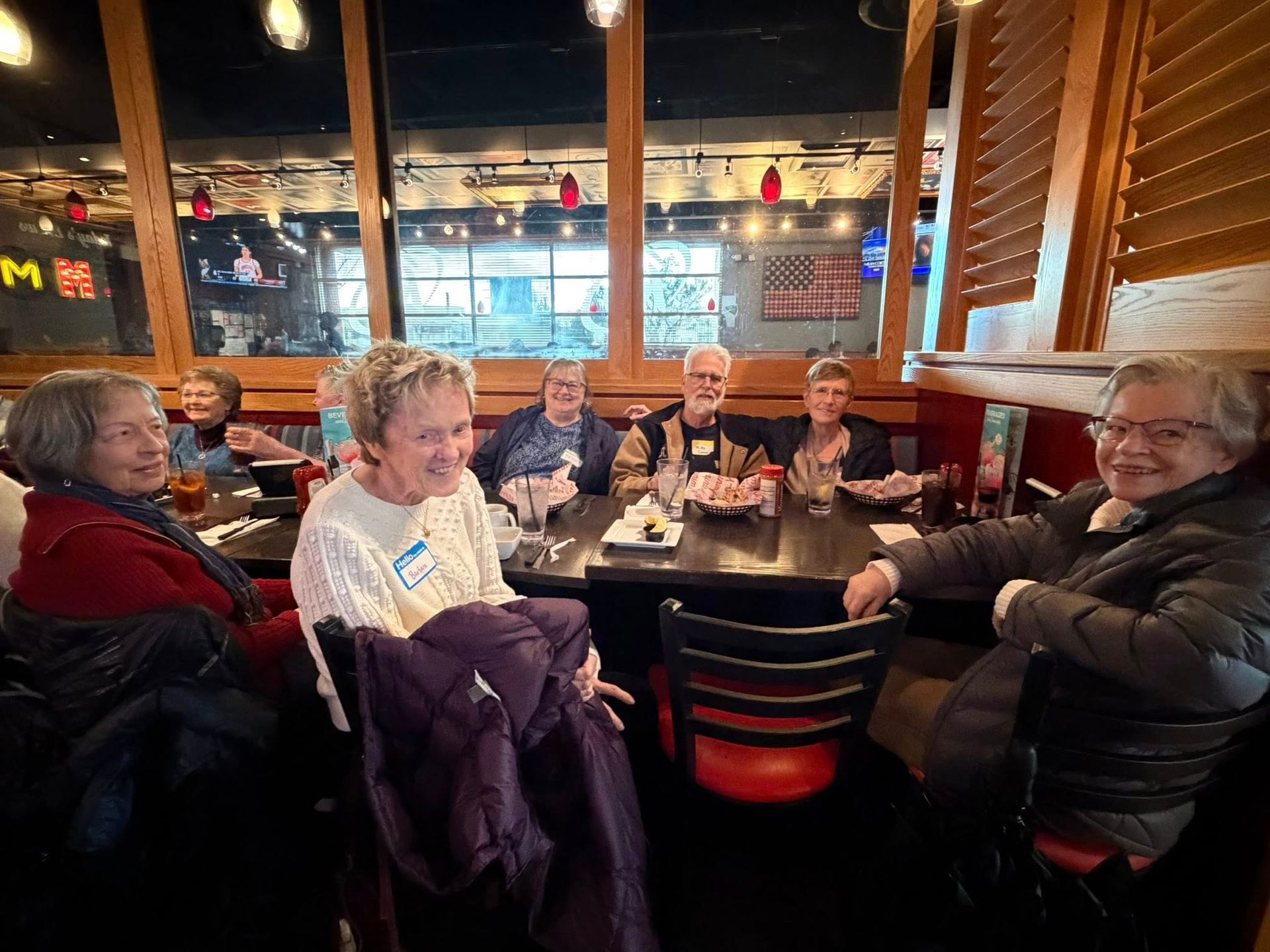 A group of people seated around a table in a cozy restaurant with warm lighting and large windows.
