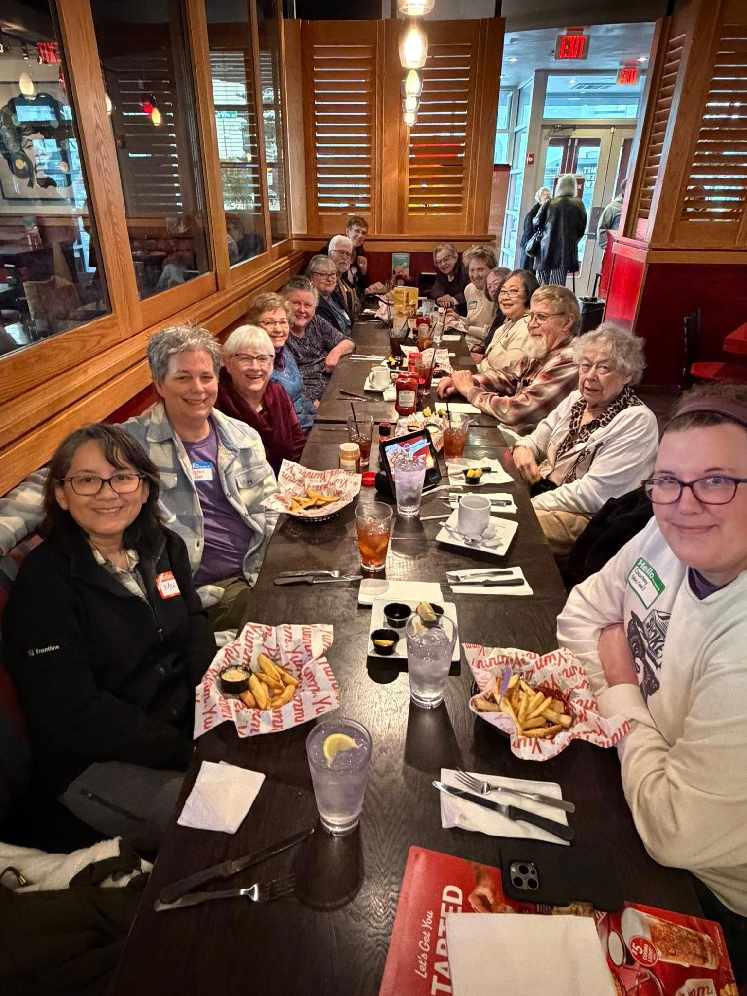 Group of friends dining together at a long restaurant table, smiling and chatting over drinks and dessert.