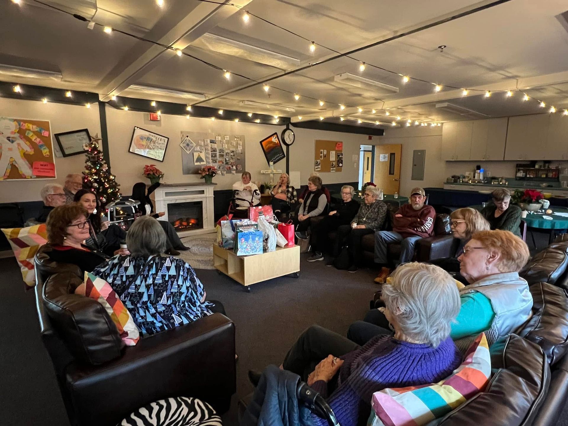 People seated in a cozy living room, gathered in a circle for a meeting or holiday celebration.