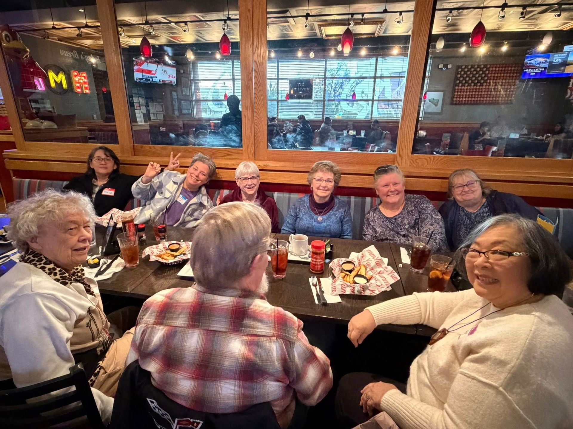 Group of people gathered around a restaurant table, smiling and chatting with drinks and plates.