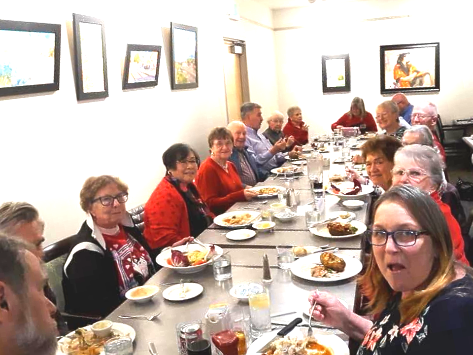 People seated at a long restaurant table, eating and talking together.
