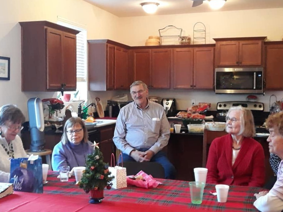 People seated around a table in a kitchen, chatting during a small gathering.