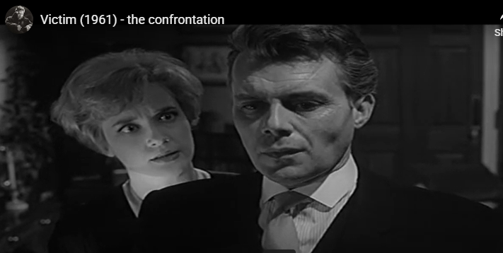 Black-and-white film still: two serious people in close-up during a confrontation indoors.