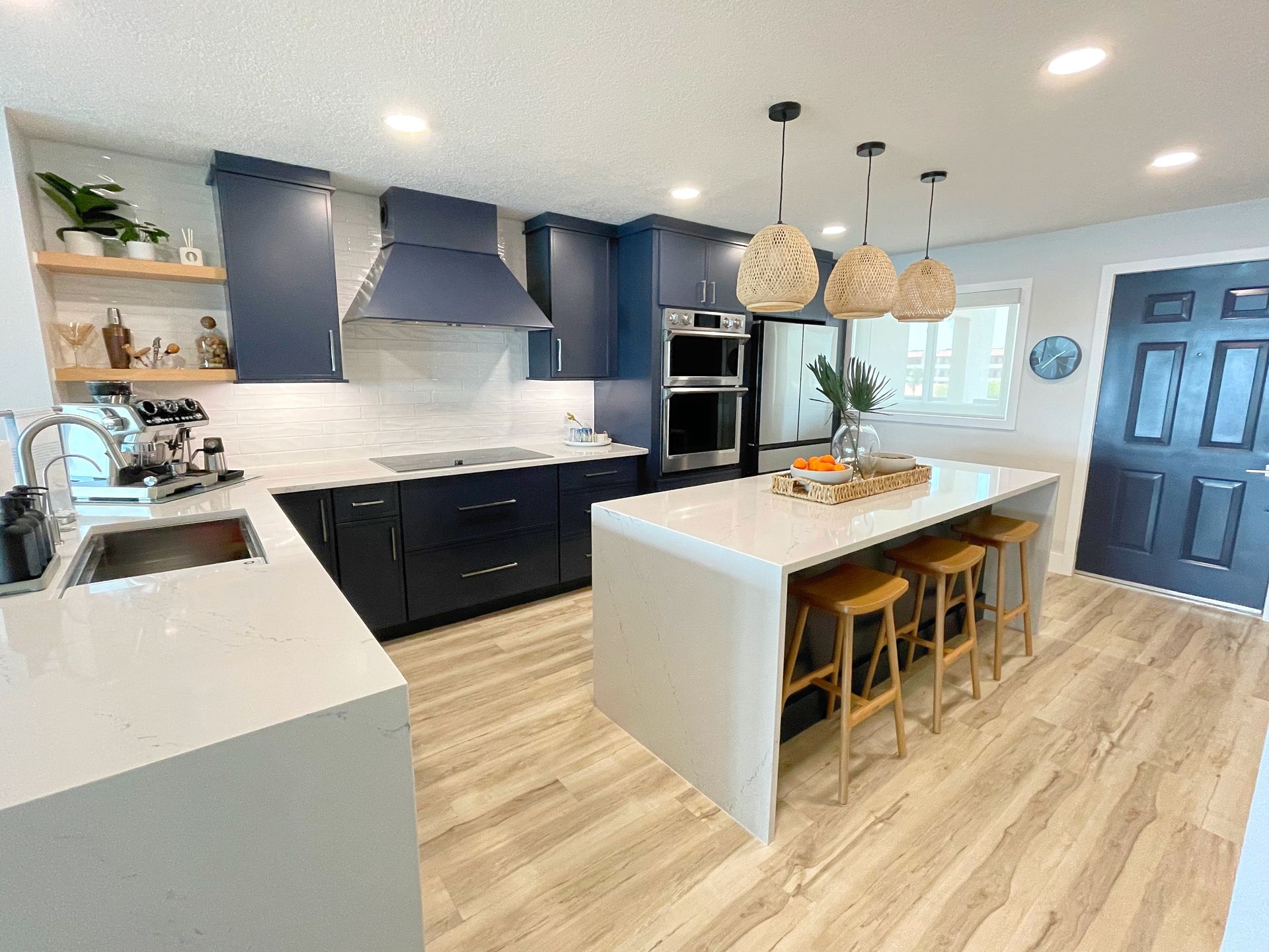 Modern kitchen with navy cabinets, white island, light wood floors, and pendant lights