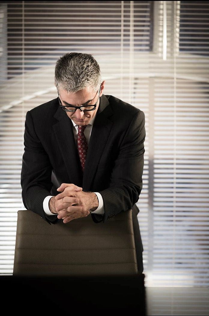 A man in a suit and tie is sitting at a desk with his hands folded.