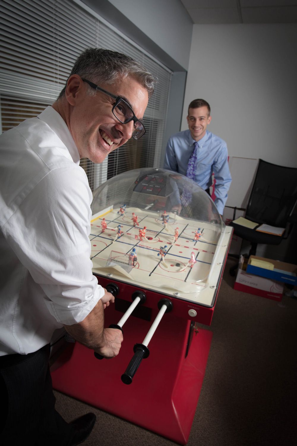 Two men are playing a foosball game in an office.