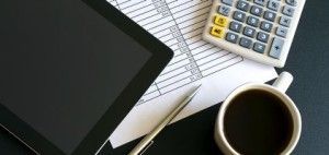 A cup of coffee , a pen , a tablet , and a calculator are on a table.