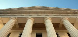 The front of a building with columns and a blue sky in the background.