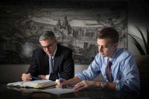 Two men are sitting at a table looking at a book.