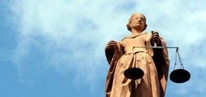 A statue of a woman holding a scale in front of a blue sky.