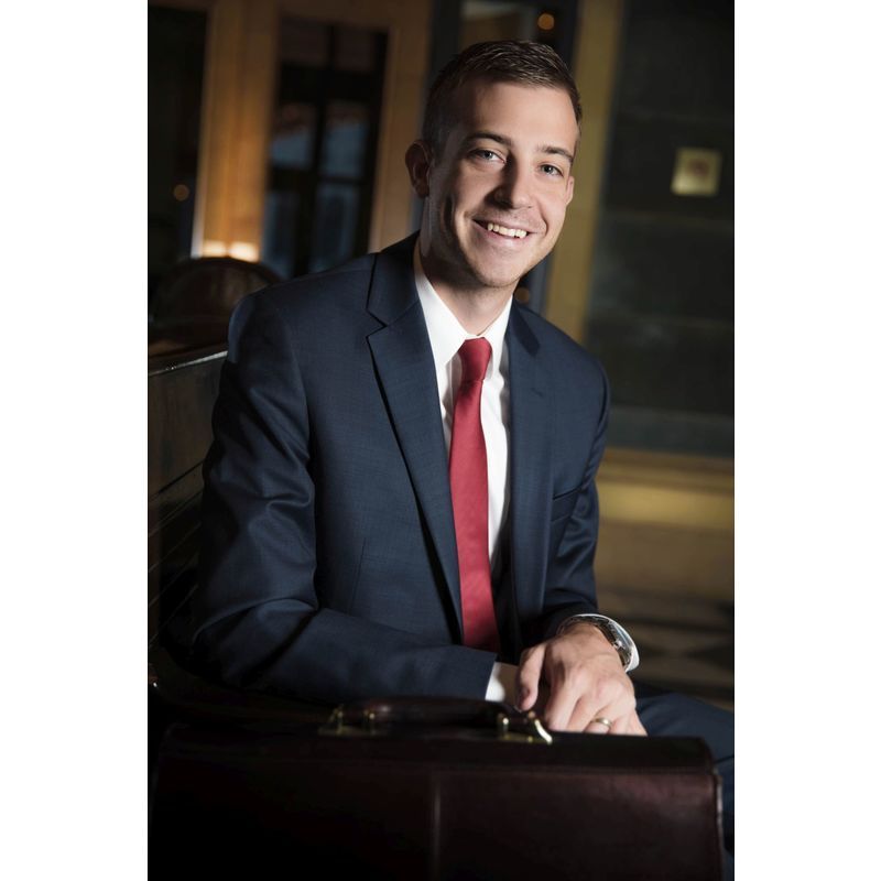 A man in a suit and tie is holding a briefcase and smiling.