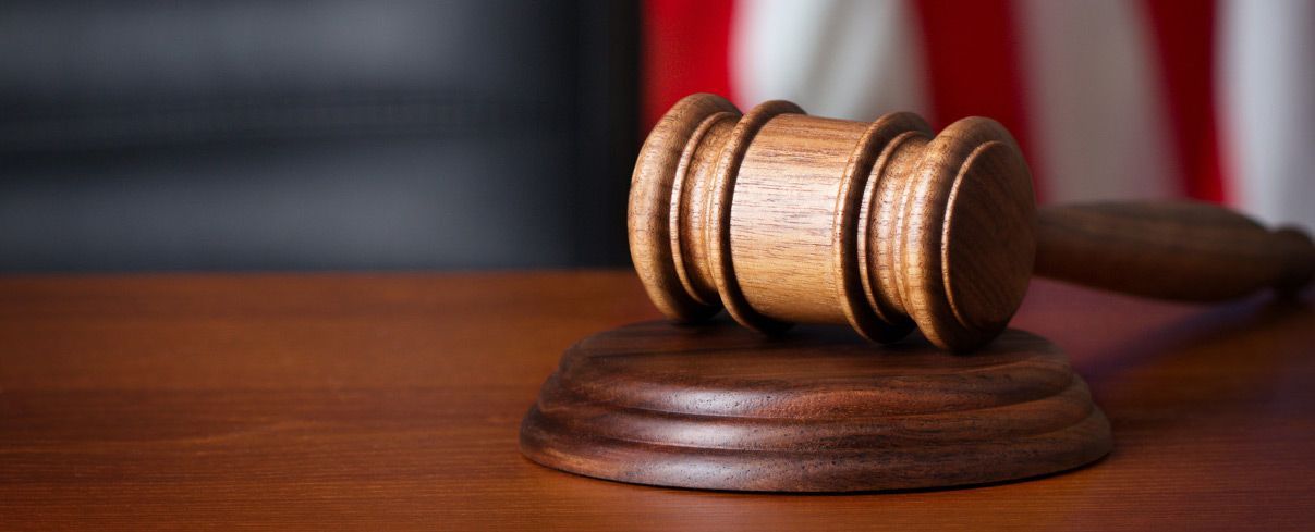 A wooden judge 's gavel is sitting on a wooden table in front of an american flag.