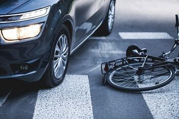 A bicycle is laying on the ground next to a car at a crosswalk.
