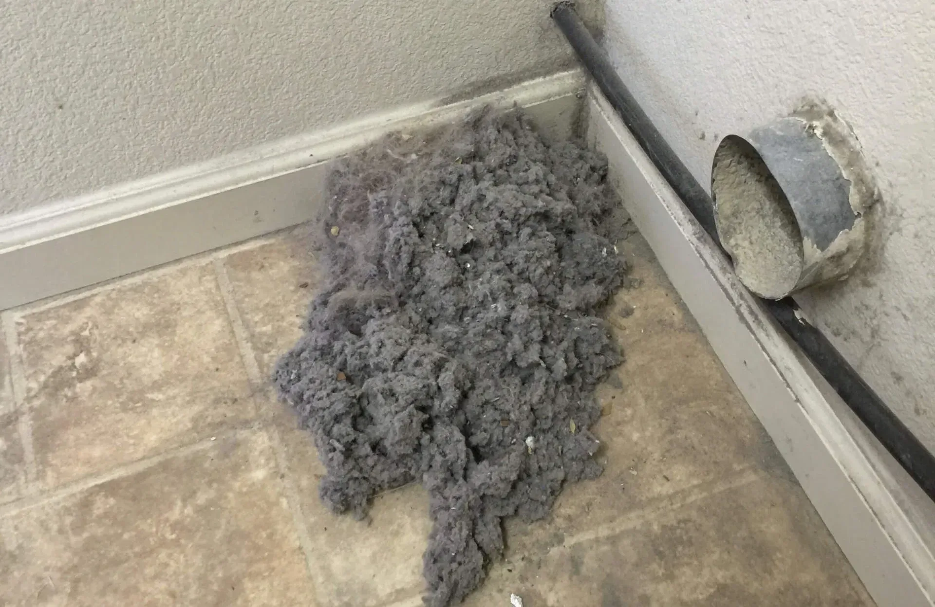 Gray lint pile on a tiled floor beside a wall vent and baseboard. Gray lint pile on a tiled floor beside a wall vent and baseboard.