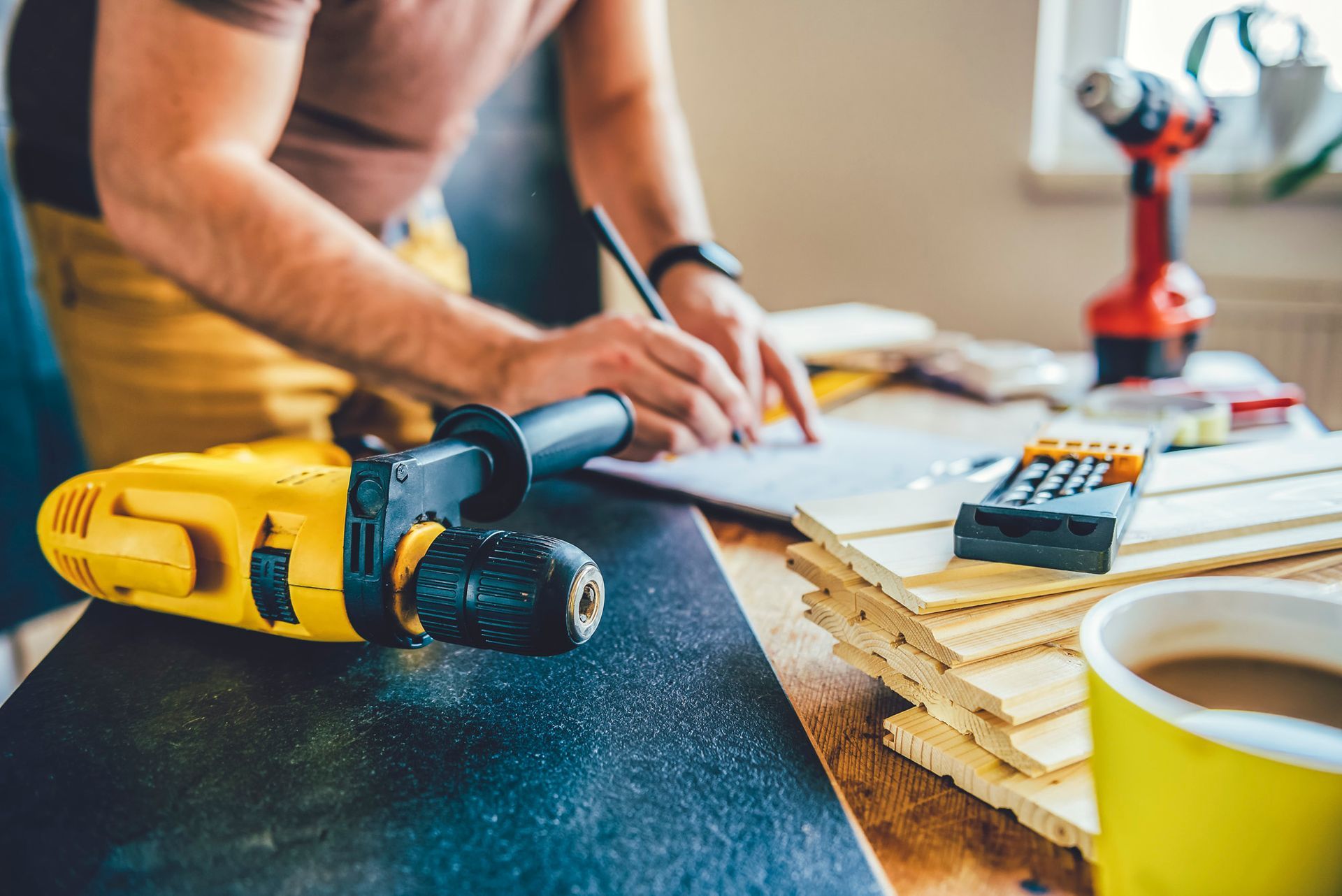A man is sitting at a table with a drill and a cup of coffee.