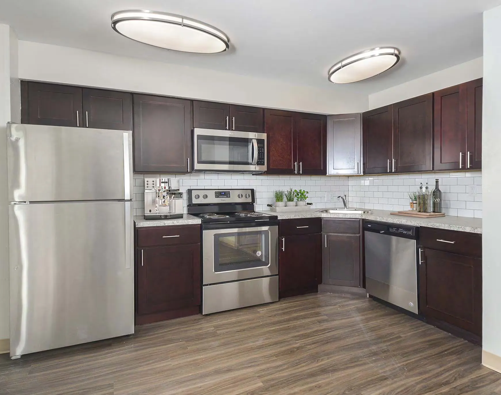 Modern kitchen with stainless steel appliances, dark cabinets, and light wood-look flooring.