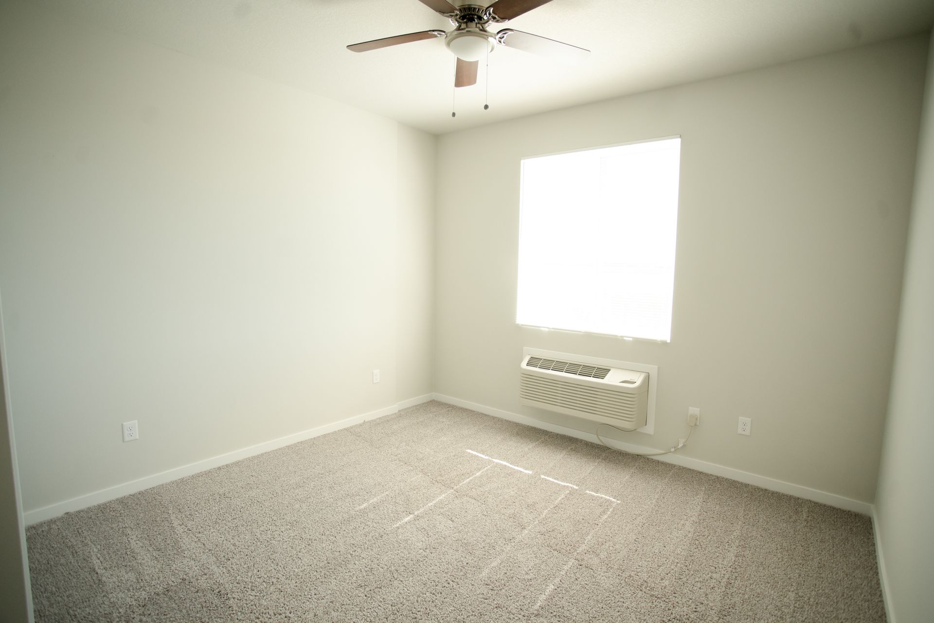 An empty bedroom with a ceiling fan and a window.