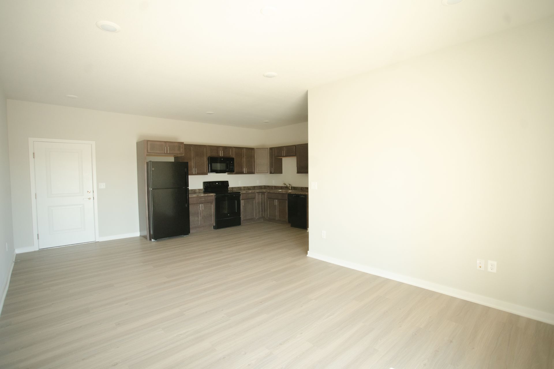 An empty living room with a kitchen in the background.