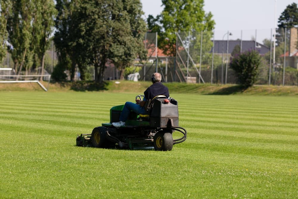 A Man is Riding a Lawn Mower on a Lush Green Field — Land to Mow Garden Services Wagga In Junee, NSW