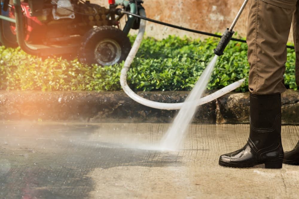 A Man is Using a High Pressure Washer to Clean a Sidewalk — Land to Mow Garden Services Wagga In Wagga Wagga, NSW