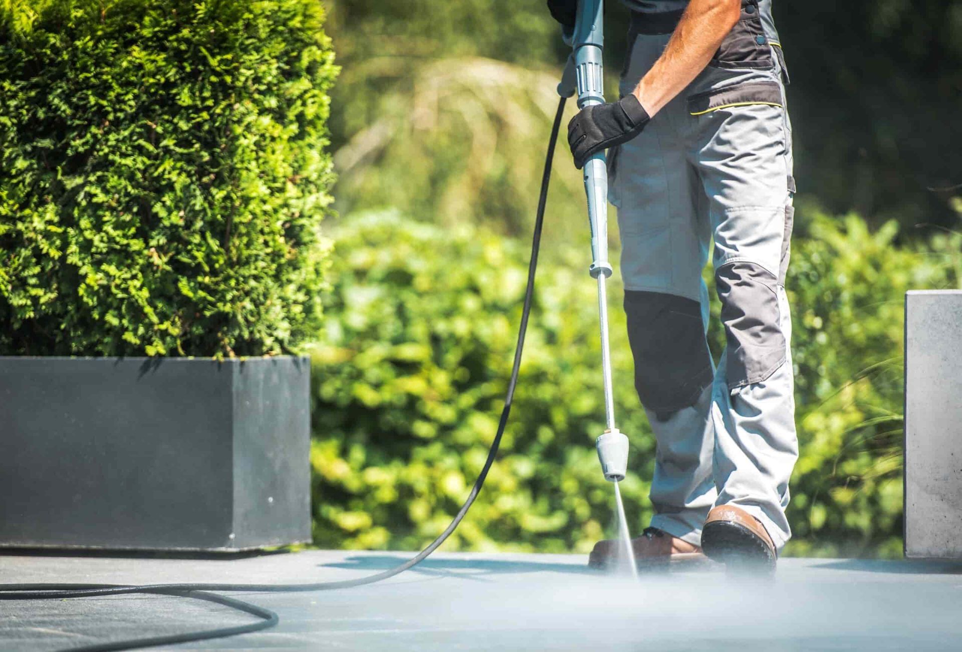 A Man is Using a High Pressure Washer to Clean a Patio — Land to Mow Garden Services Wagga In Wagga Wagga, NSW