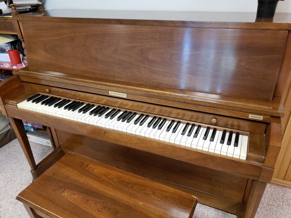 Wooden upright piano with bench; keys visible, indoors.