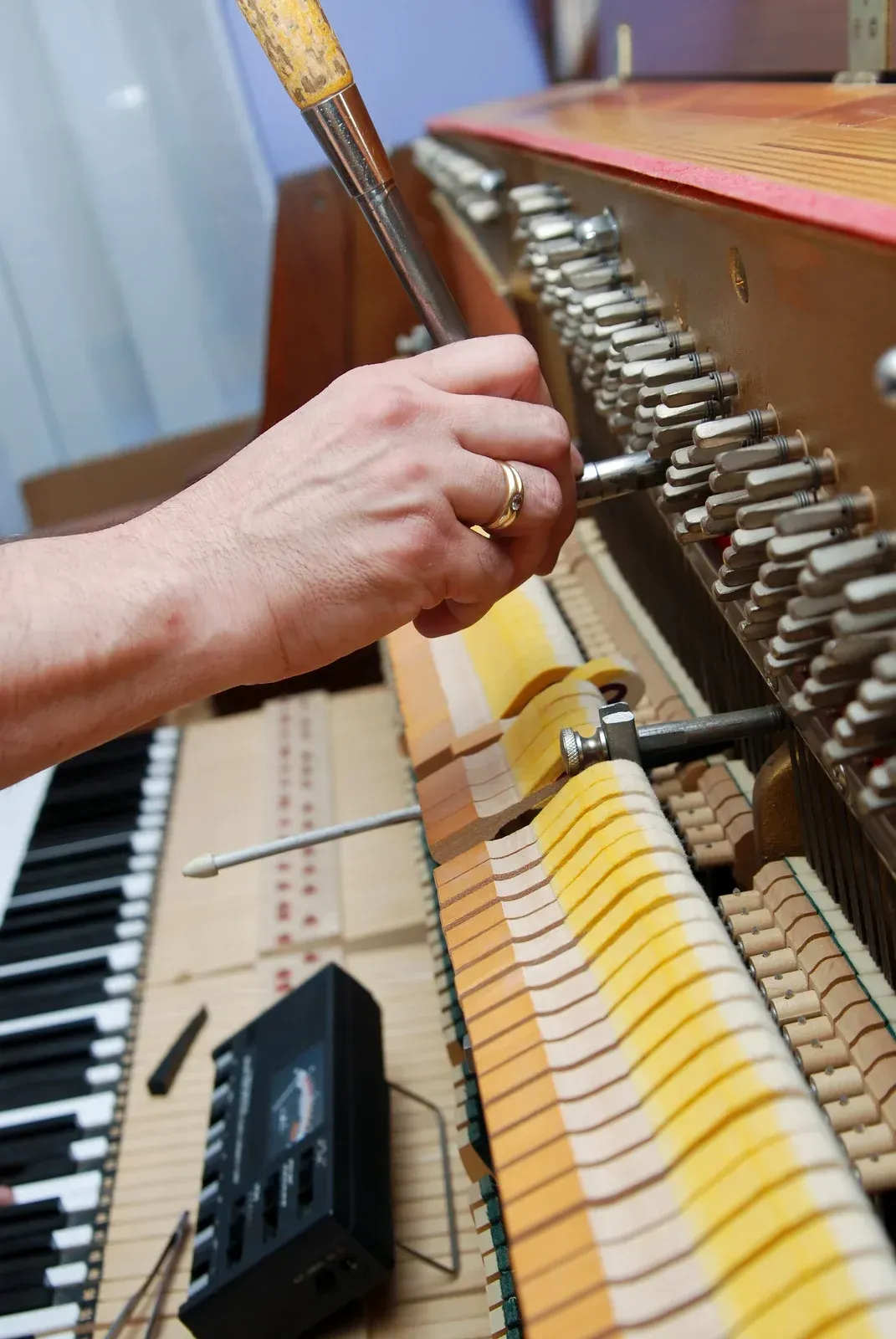 Person tuning piano with a tool, close-up of keys and mechanism.