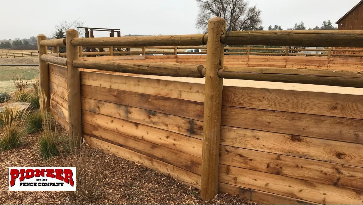 A wooden fence surrounds a sandy area with trees in the background.