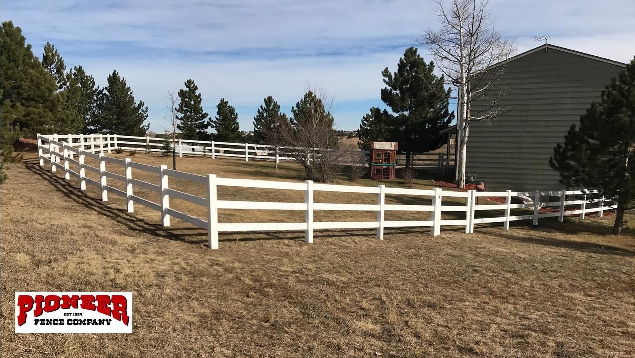 A wooden picket fence is surrounding a house on the side of the road.